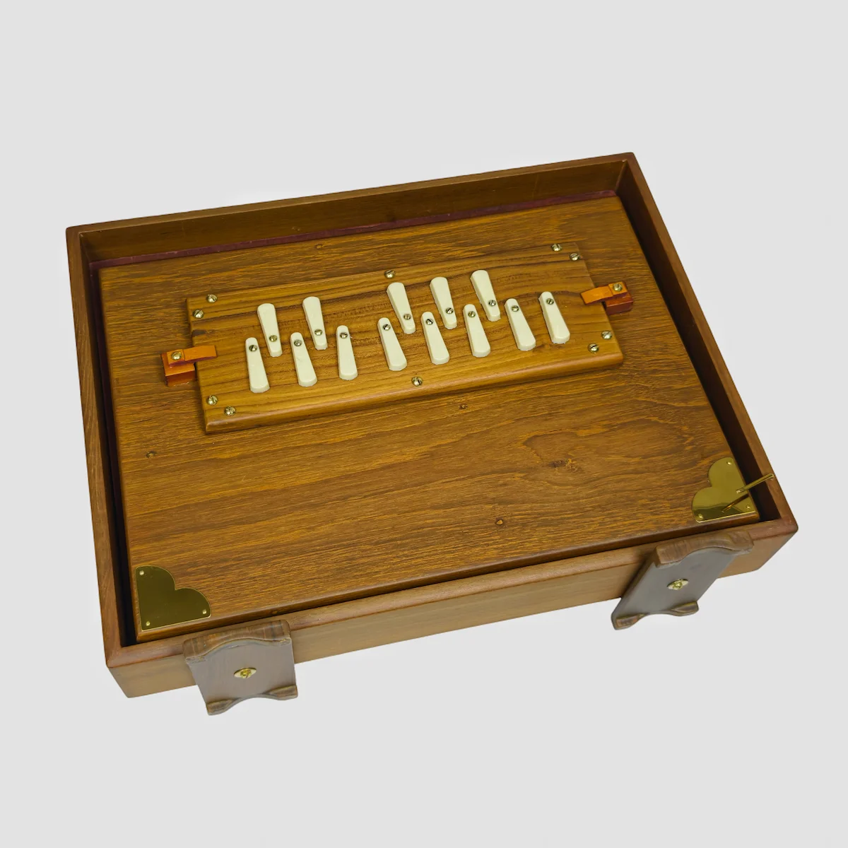Lower side view of a closed teak shruti box displaying natural wood grain and stable wooden feet